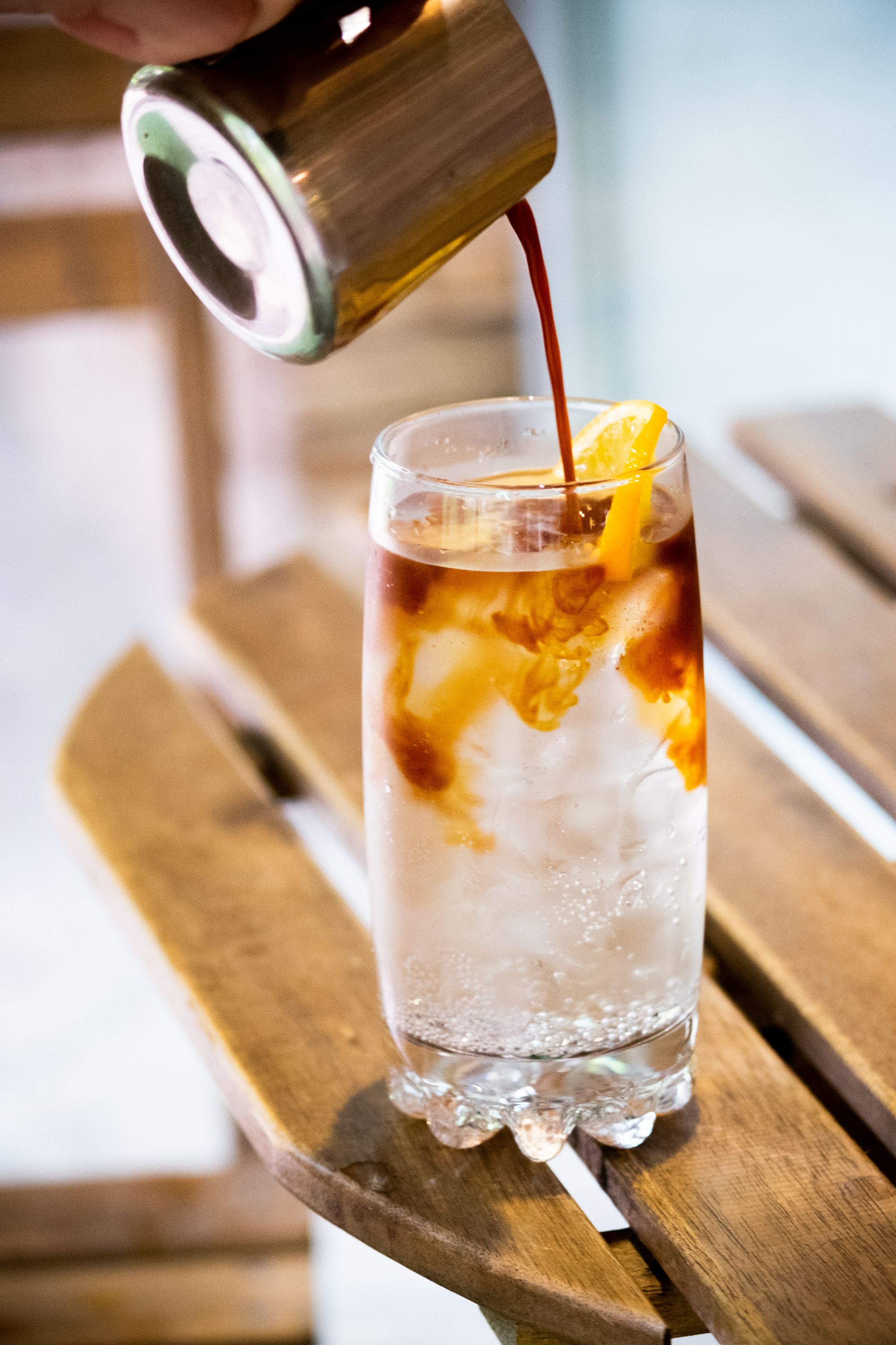 Coffee being poured into a sparkling citrus tonic over ice
