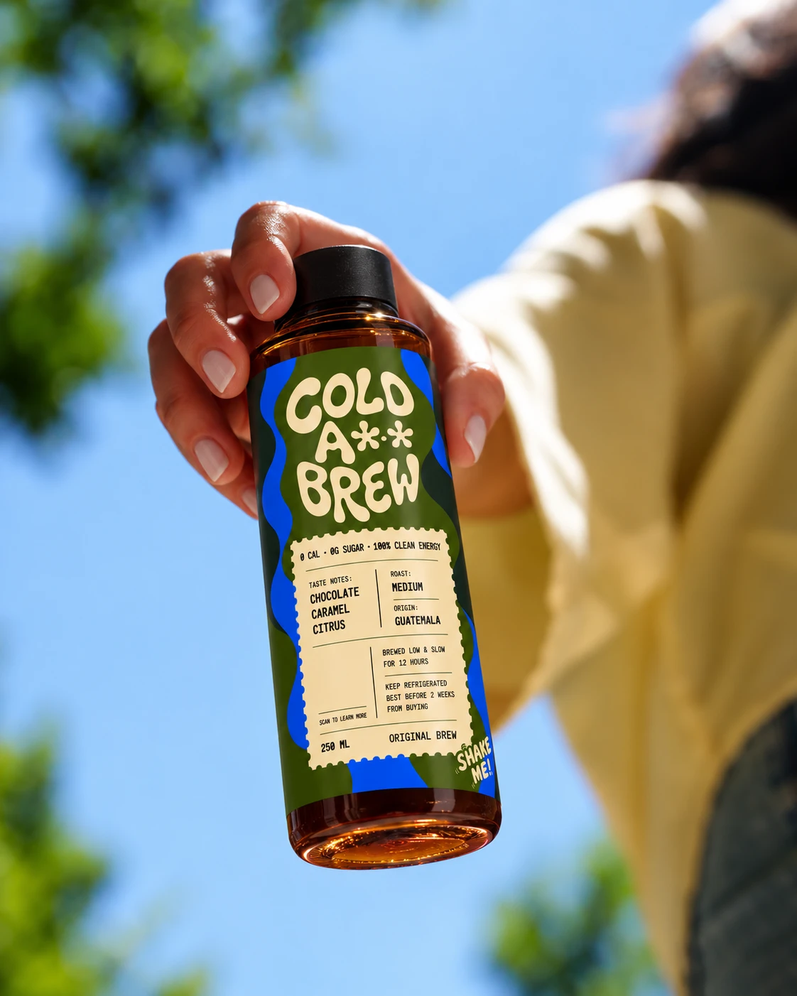 A hand holding a bottle of Cold A** Brew up against a clear blue sky
